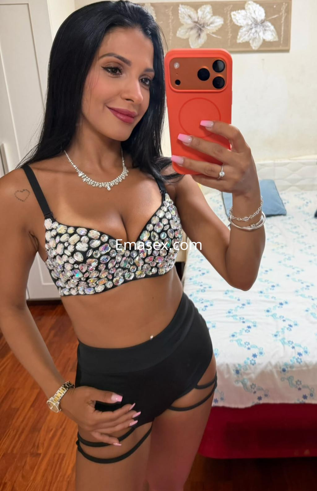 Escort en Donosti, vistiendo un top brillante y shorts negros, posando frente a un espejo con una sonrisa.