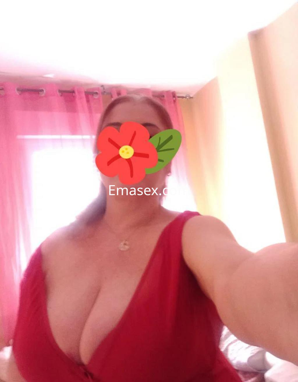 Escort en Toledo con cabello largo y rubio, viste un vestido rojo que resalta su figura en un entorno luminoso.