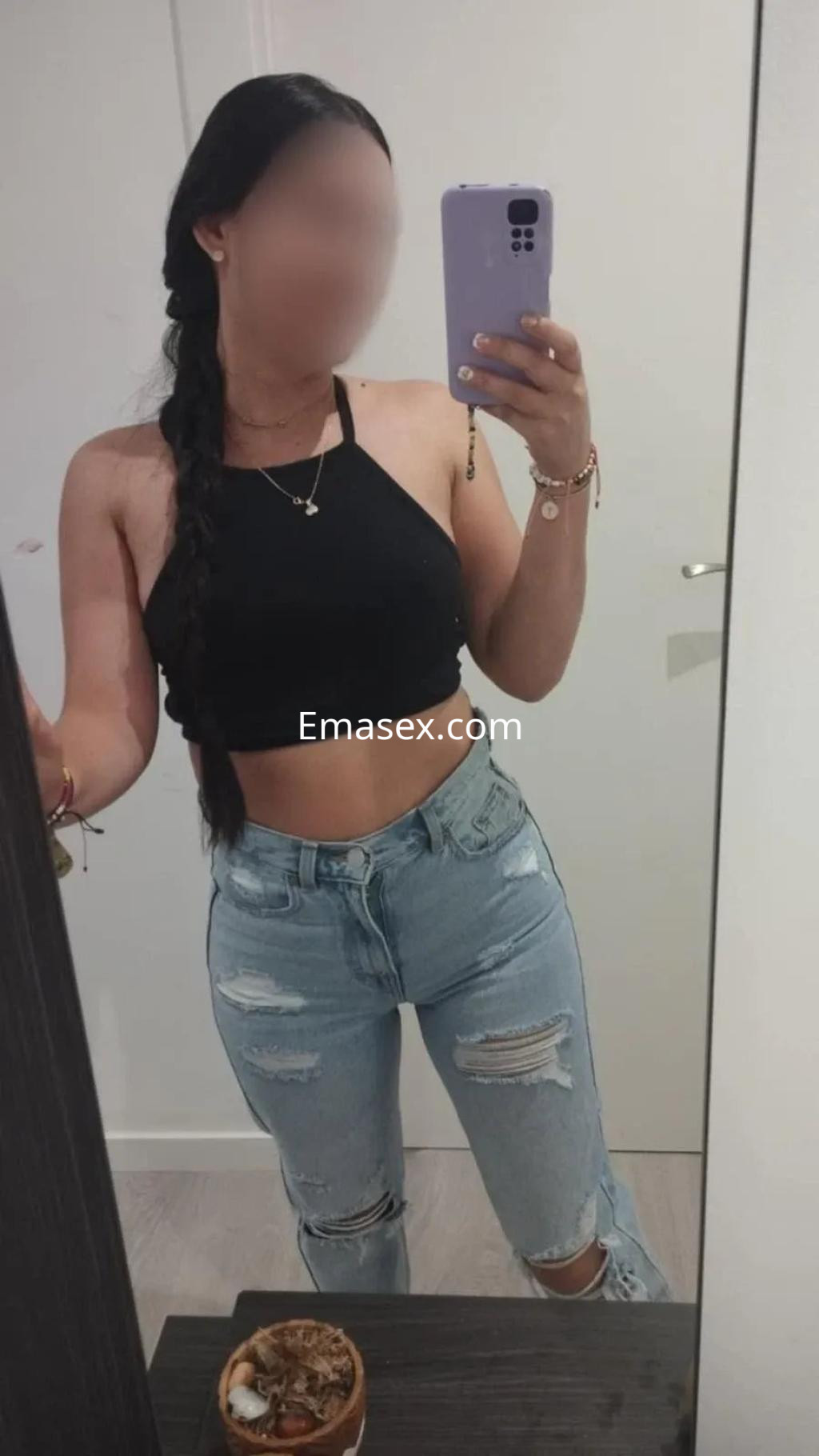 Escort en Albacete con blusa negra ajustada y jeans rotos, posando frente al espejo con una trenza.