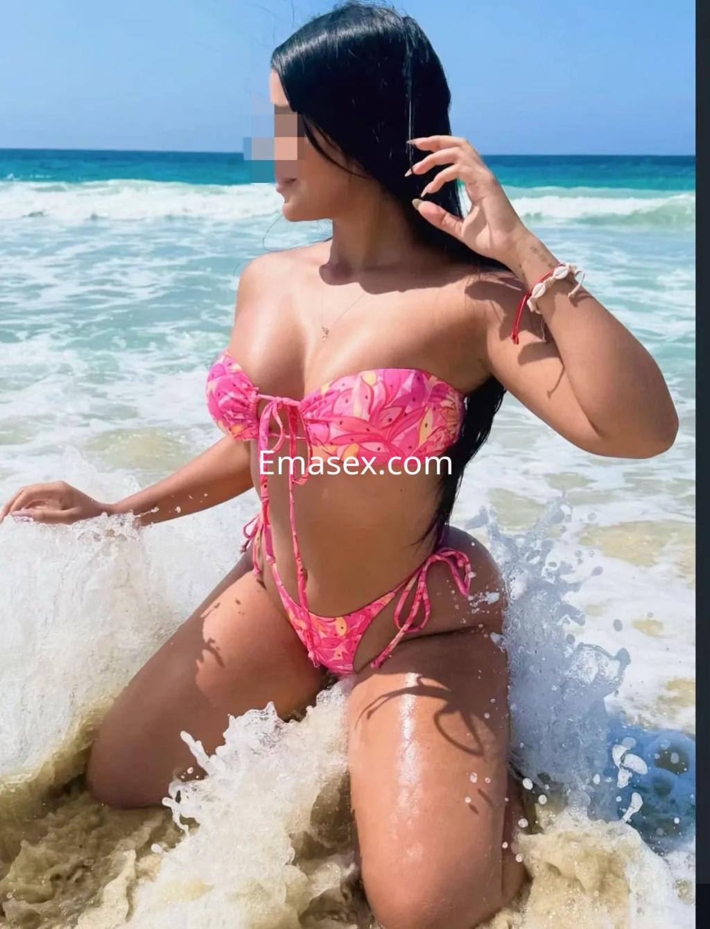 Escort en Albacete con bikini rosa, posando en la orilla del mar mientras juega con el agua y su cabello.