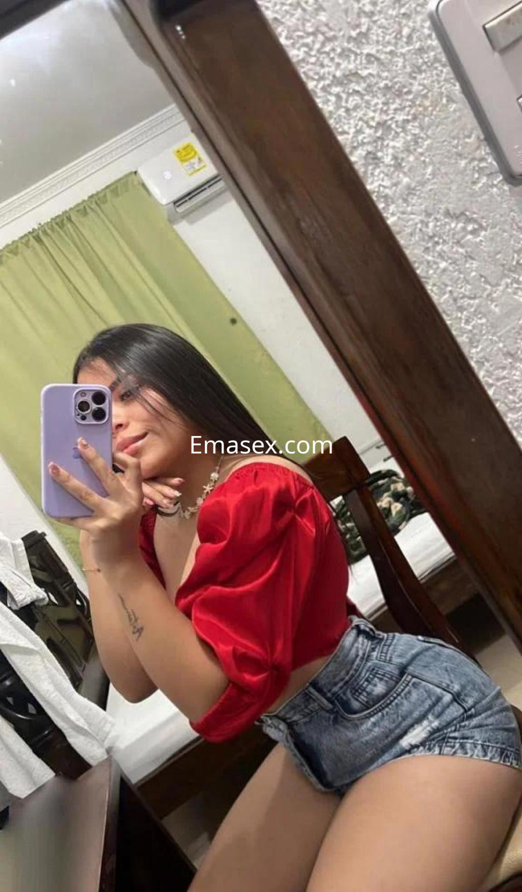 Puta en Burgos posando con una blusa roja y shorts de mezclilla, con cabello largo y lacio frente al espejo.