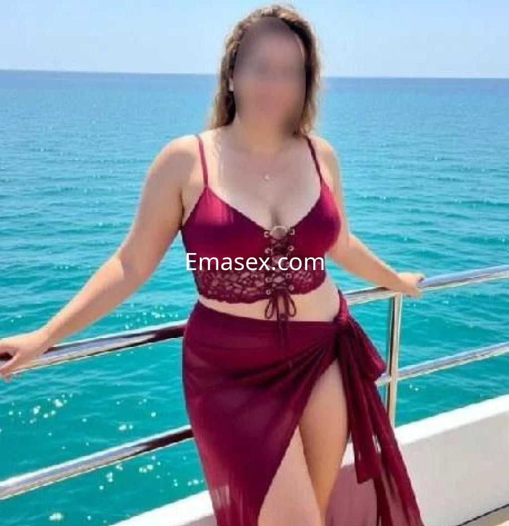 Escort en Cáceres posando junto al mar, con un bikini burdeos y una falda de playa transparente.