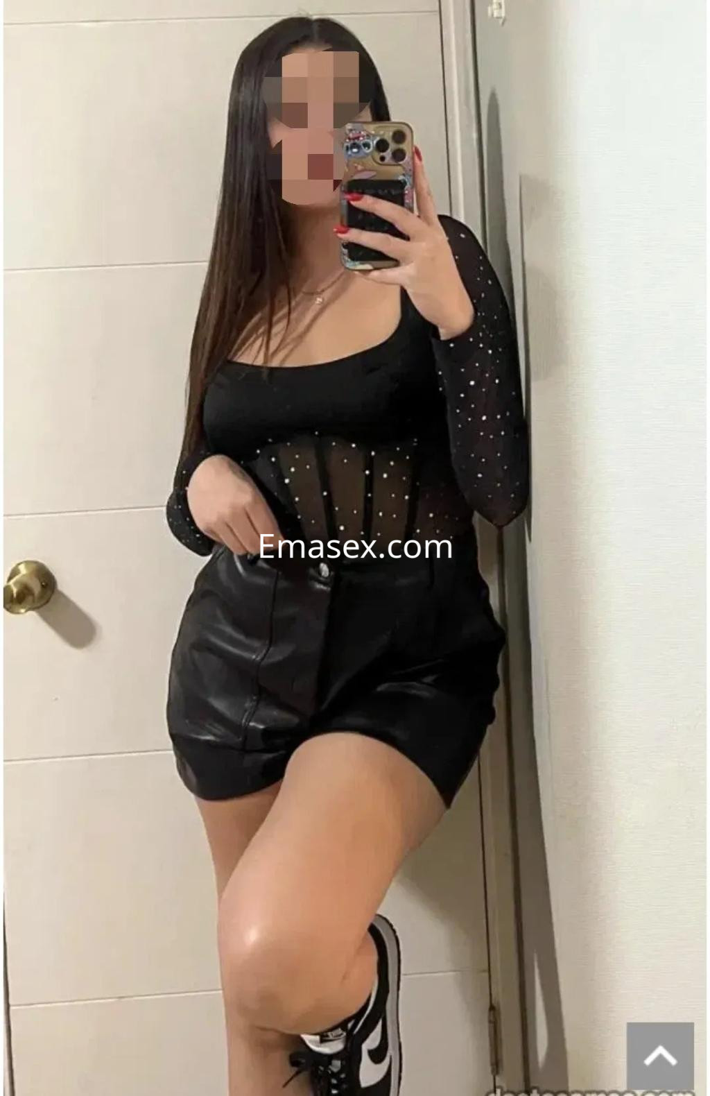 La puta muestra un atuendo negro con transparencias y un short de cuero, posando frente a un espejo en Cádiz.