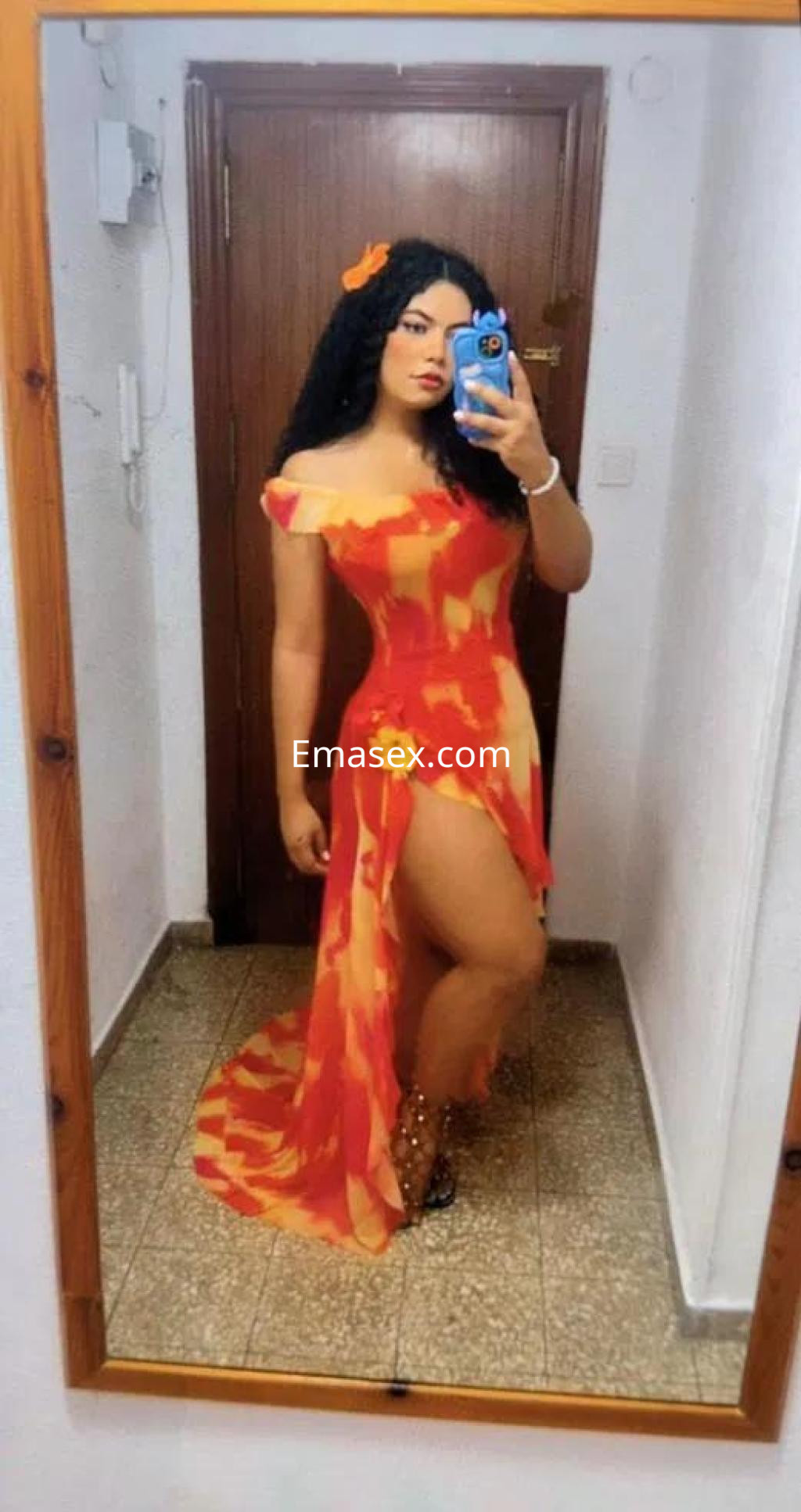 La puta en Granada se fotografía con un vestido largo de colores cálidos, mostrando una pierna y su cabello rizado.