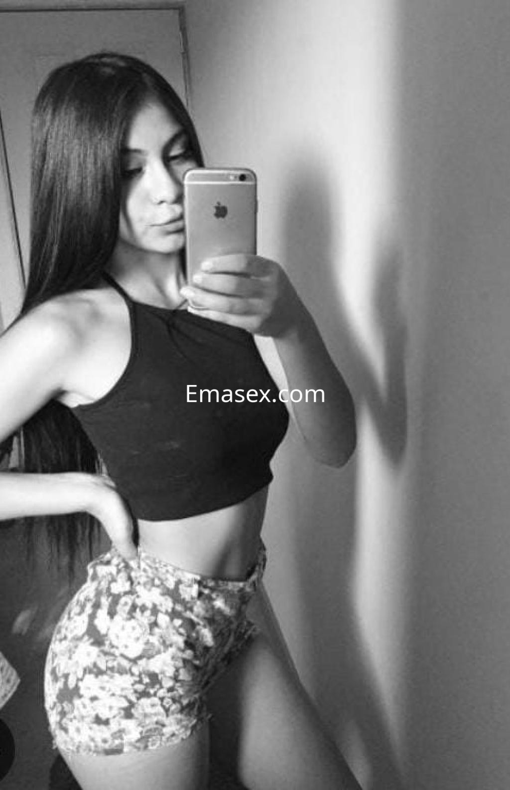 Escort en Bilbao posando frente al espejo con blusa negra y shorts de flores, mostrando su figura esbelta.