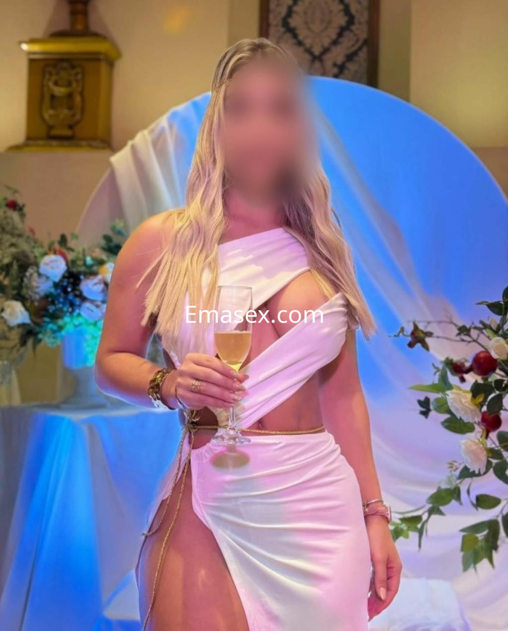 Escort en Córdoba sosteniendo una copa de champán, con un vestido blanco ajustado y cabello largo y rubio.
