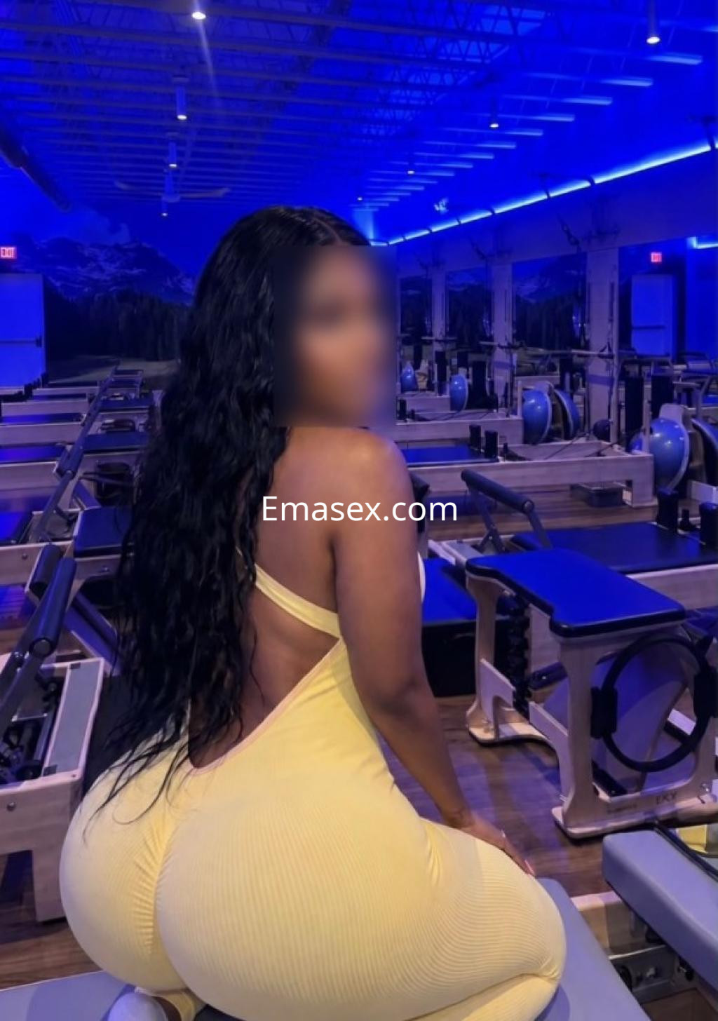 Puta en Granada con un ajustado mono amarillo, de espaldas, en un gimnasio con iluminación azul.