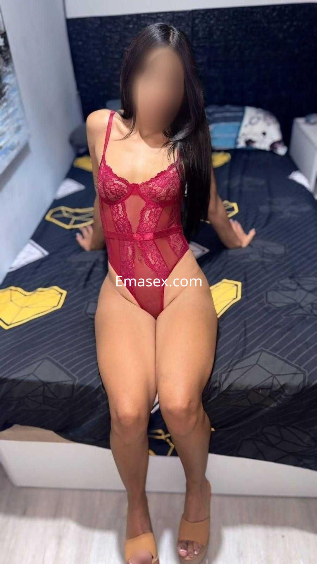 La puta viste un body rojo con encaje, posando de pie sobre una cama en un ambiente de Madrid.