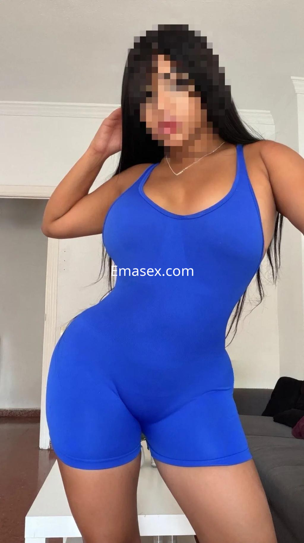 Escort en Málaga con body ajustado de color azul, cabello largo y lacio, posando en un entorno interior.