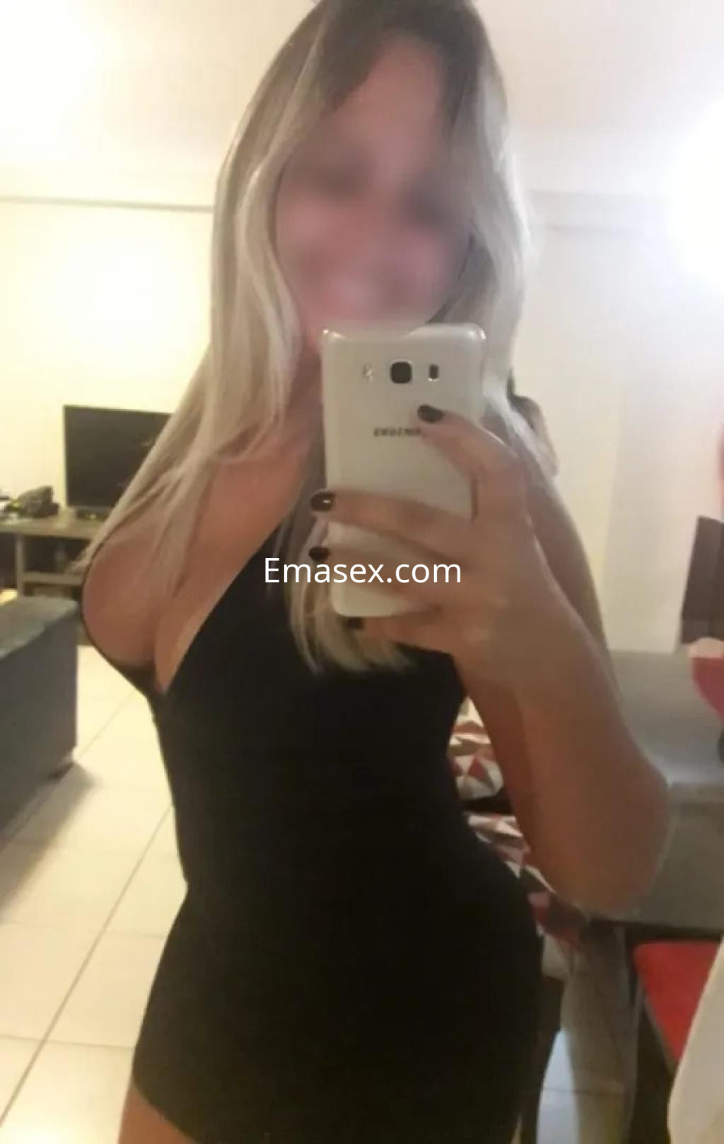 Escort en Oviedo, con vestido negro ajustado y cabello rubio, posando frente a un espejo en un ambiente moderno.