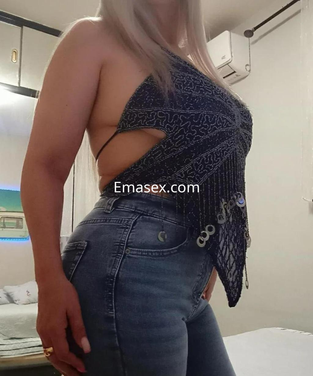 La puta muestra una pose lateral, luciendo un top adornado y jeans ajustados en un ambiente interior en Madrid.