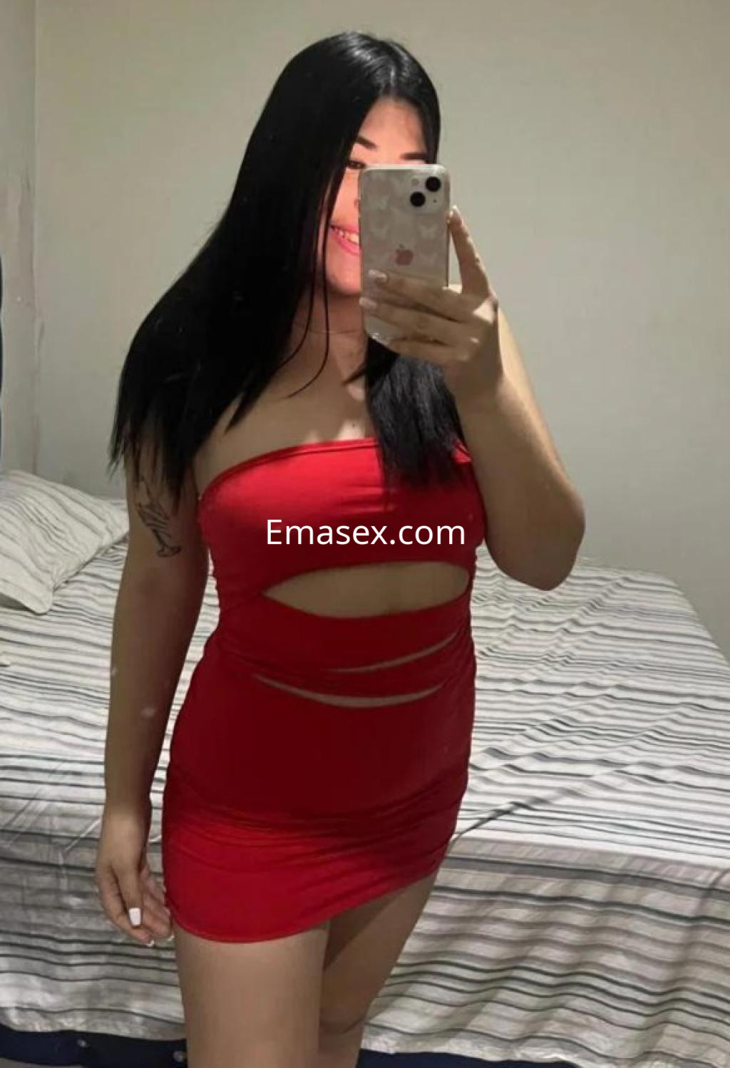 Puta en Valladolid con vestido rojo ajustado y cortes, posando en un ambiente interior con cama al fondo.