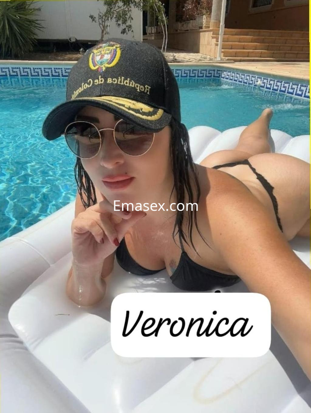 Escort en Irún con cabello oscuro, usando un bikini negro y gafas de sol, relajándose en una piscina.