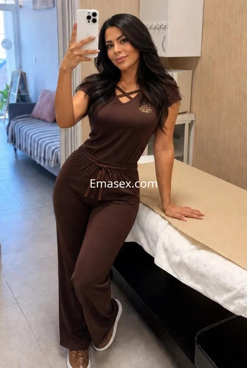Escort en Málaga posa con un conjunto marrón de estilo casual, mostrando una sonrisa mientras se apoya en una mesa.