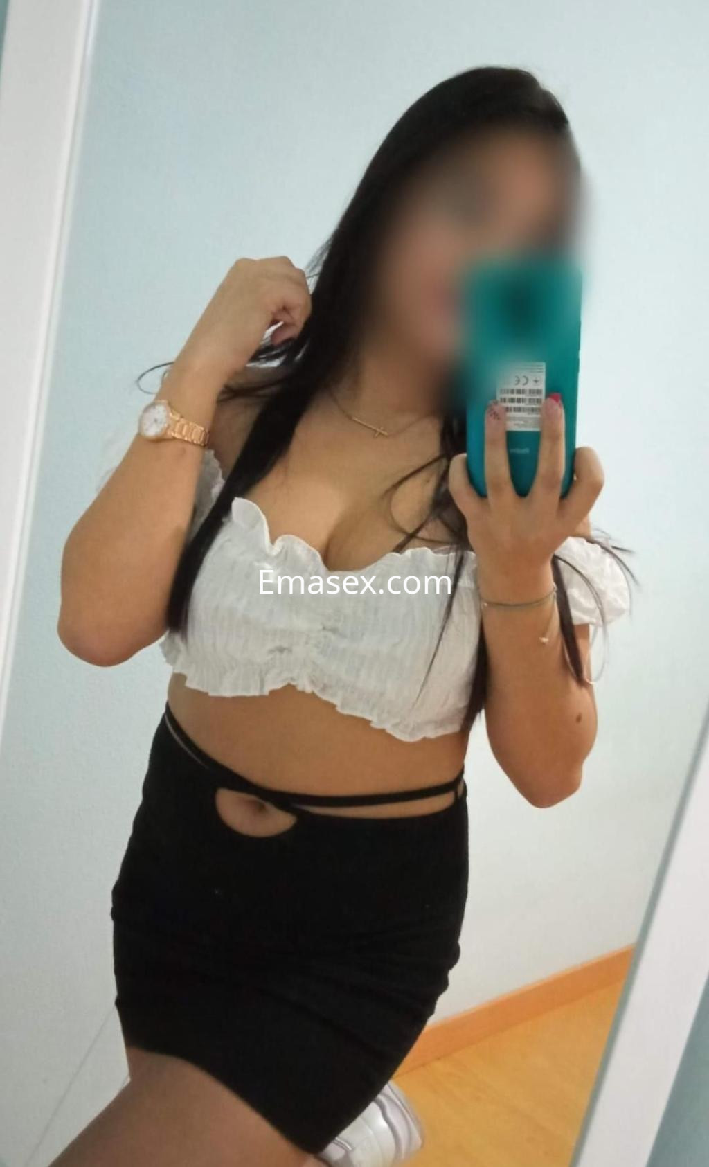 La puta en Alicante se muestra frente al espejo con blusa blanca y falda negra ajustada.