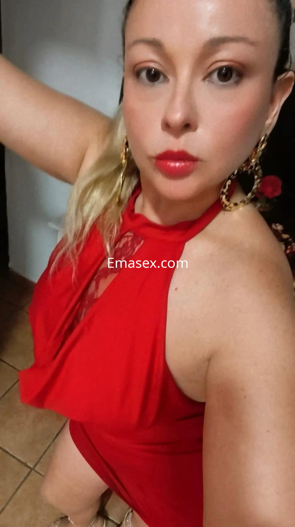 Escort en Cádiz con vestido rojo ajustado, cabello recogido y aretes grandes, posando en un ambiente interior.
