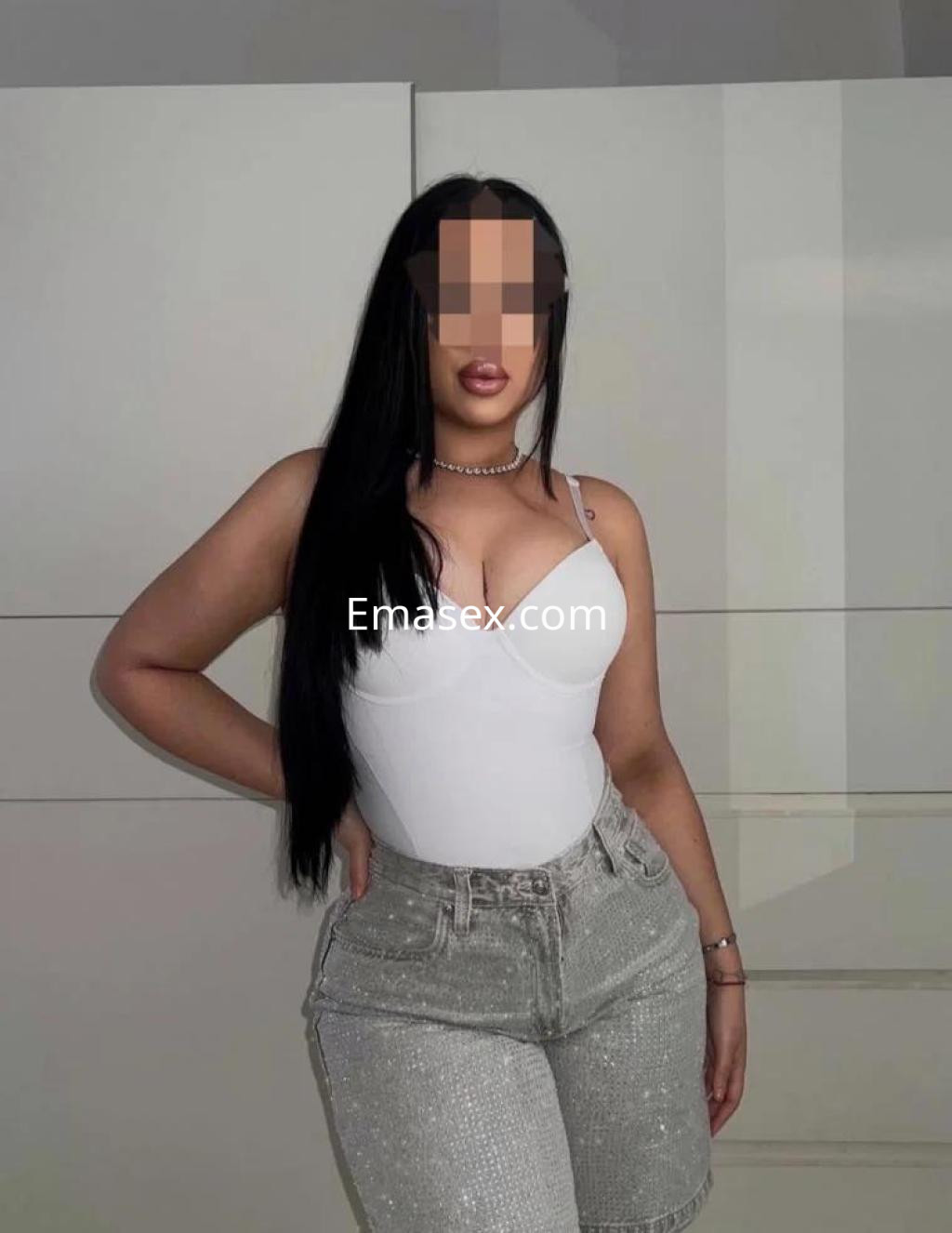 Escort en Cádiz con cabello largo y lacio, vistiendo un body blanco y shorts brillantes de denim.