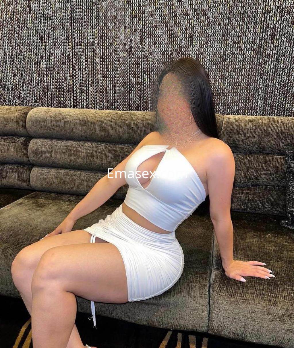 Puta con vestido blanco ajustado y escote, sentada en un sofá de terciopelo en Castellón.