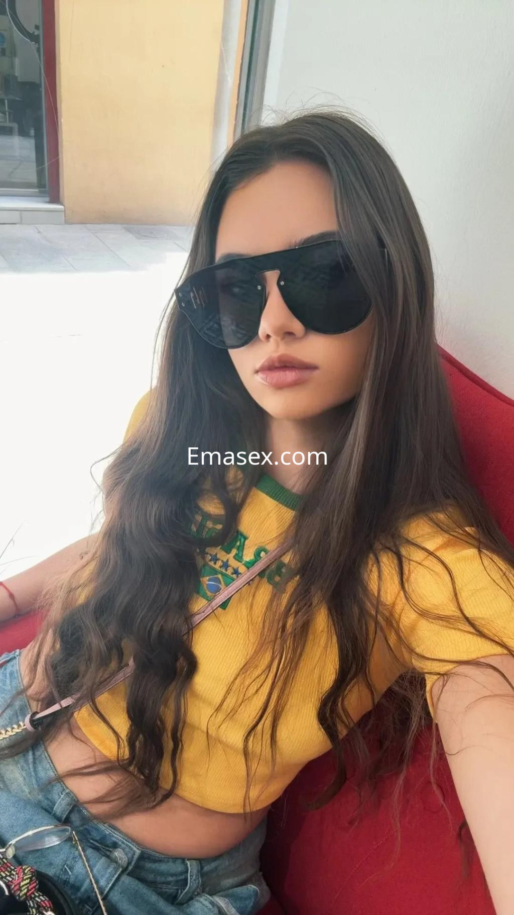 La escort en Córdoba lleva una camiseta amarilla y gafas de sol, posando con cabello largo y ondulado.