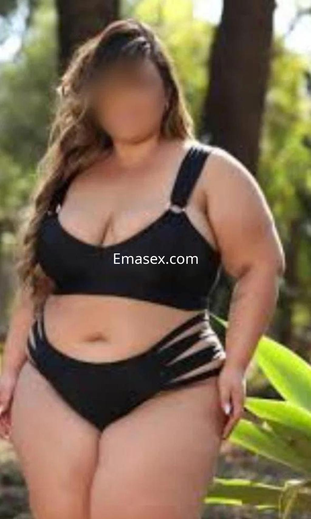 Puta con cabello largo y rizado, vistiendo un bikini negro, posando en un entorno natural en Granada.