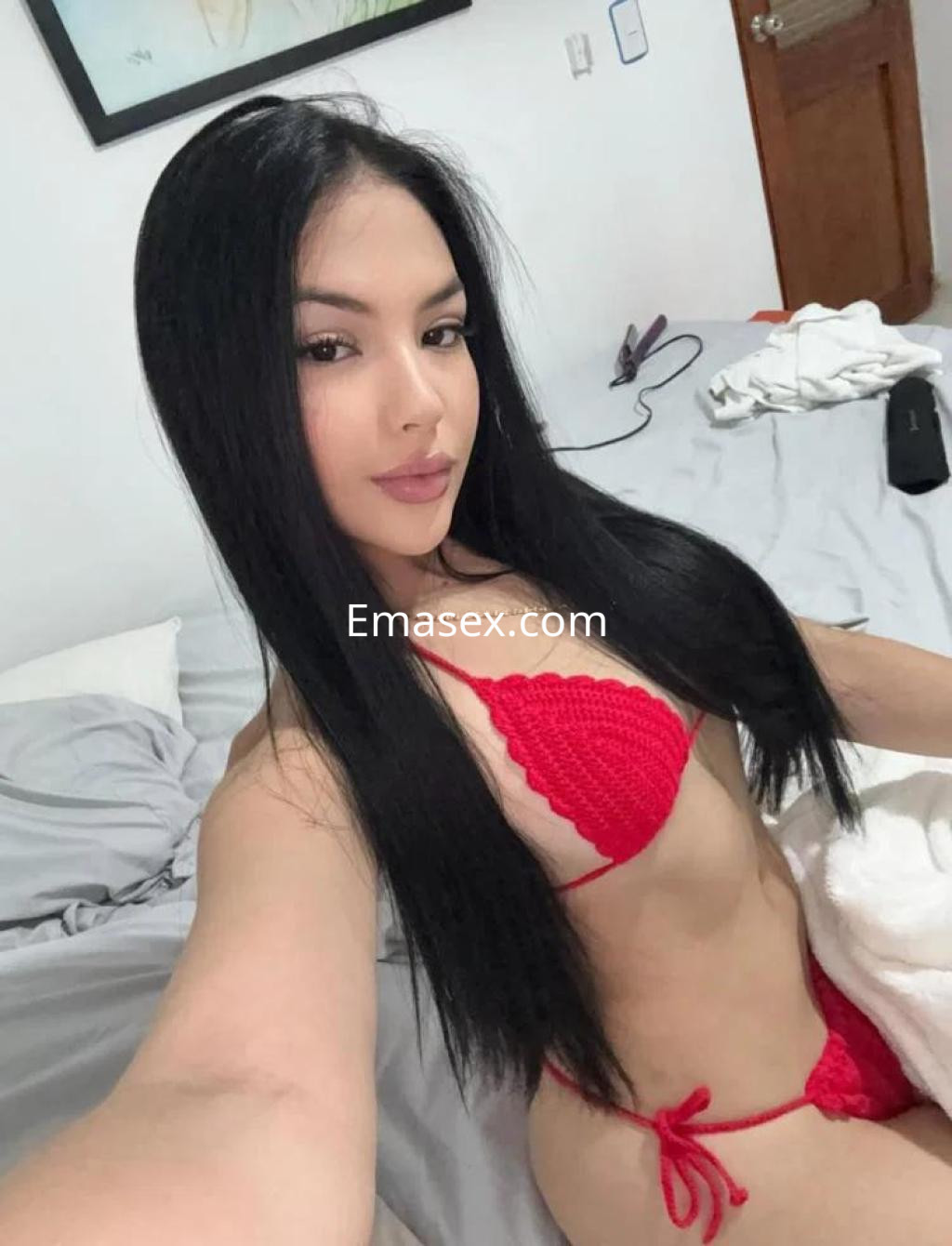 Escort en Lugo posando en la cama con un bikini rojo, cabello largo y lacio, mostrando una expresión coqueta.