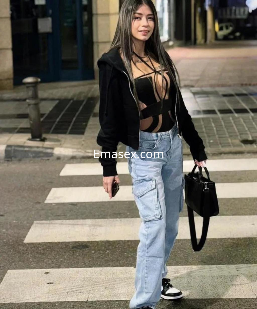 Escort en Madrid con cabello largo y lacio, usando un top negro y pantalones claros en una calle urbana.