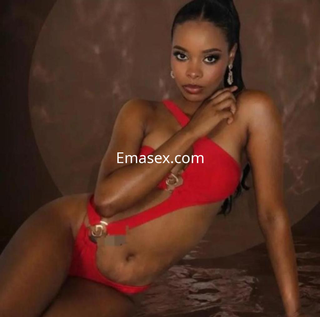 Escort posando en Ourense con un bikini rojo, joyas elegantes y un fondo en tonos marrones.