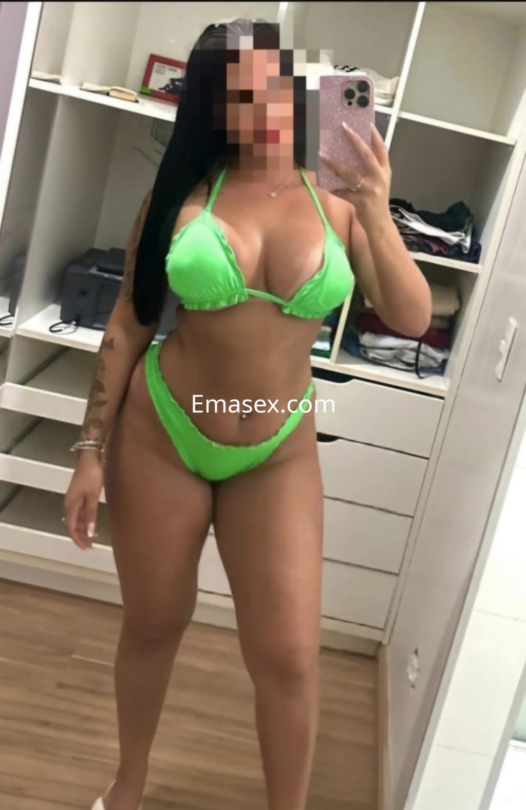 Puta de Ourense posando frente al espejo con un bikini verde, mostrando su figura y cabello largo.