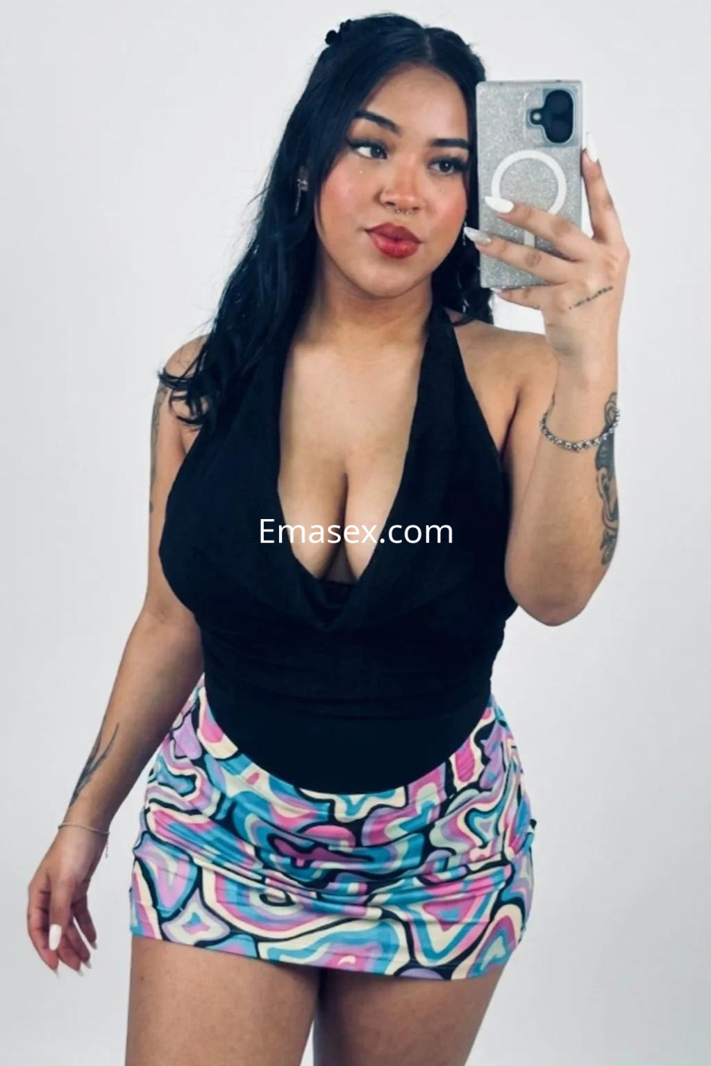 Escort en Málaga con top negro y falda corta de colores vibrantes, posando con una mano en la cadera.