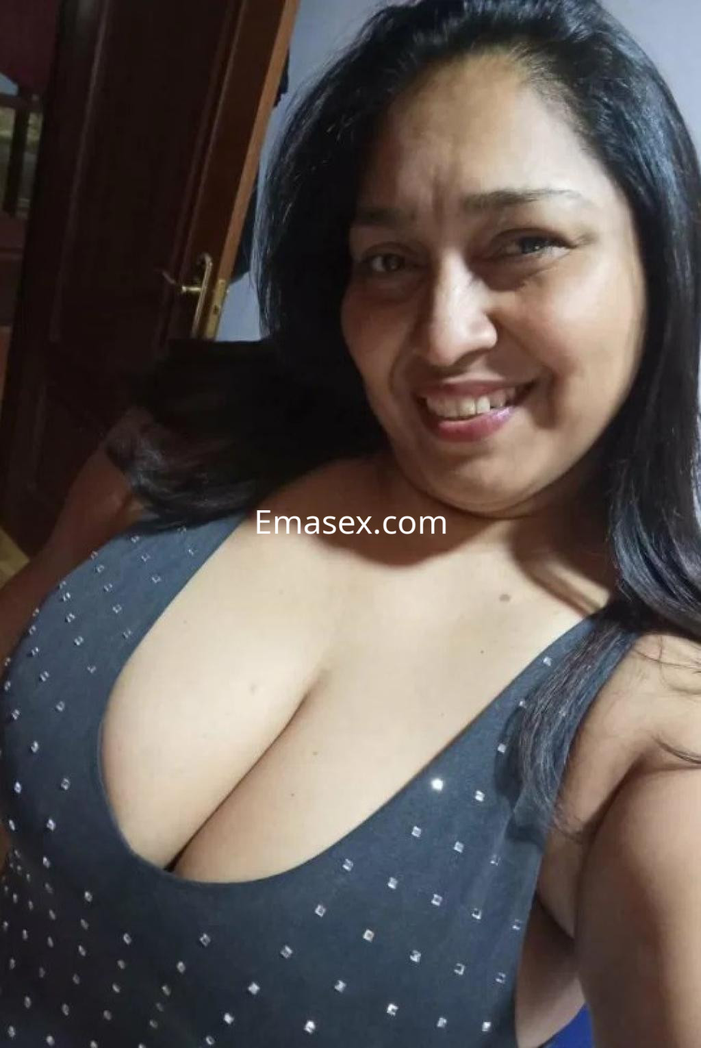 Puta en Oviedo sonríe mientras posa con un vestido negro ajustado, mostrando un escote pronunciado.