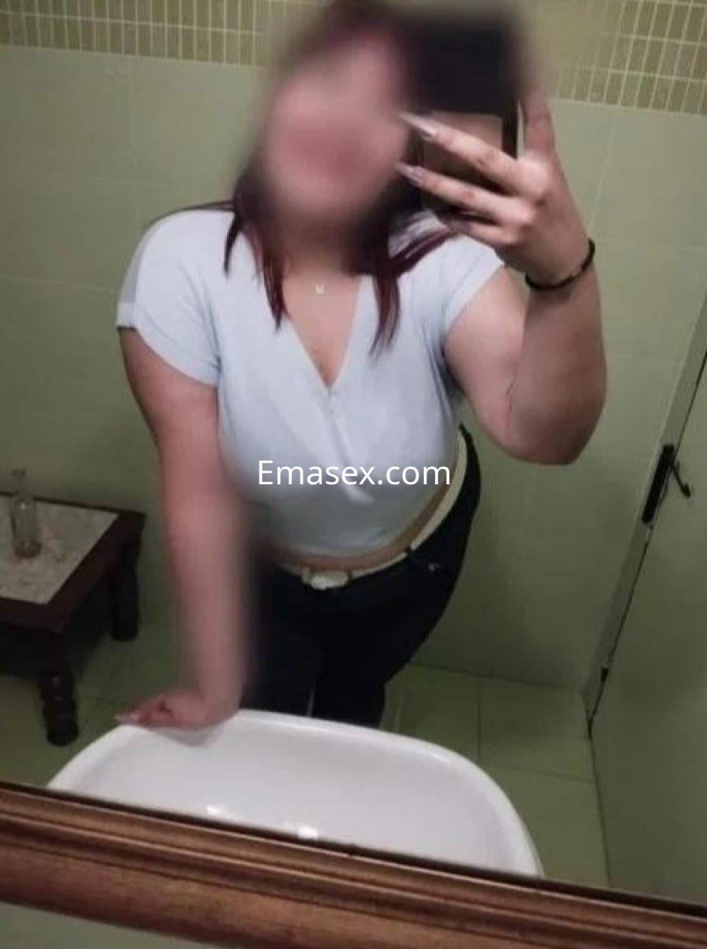 Puta en Barcelona se toma una selfie en un baño, luciendo una camiseta clara y jeans ajustados.