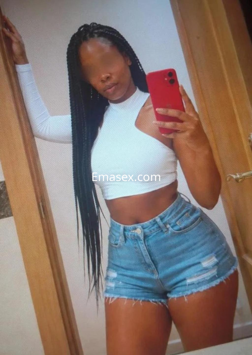 La escort en Valladolid se muestra con top blanco y shorts de mezclilla, posando frente al espejo con el cabello trenzado.
