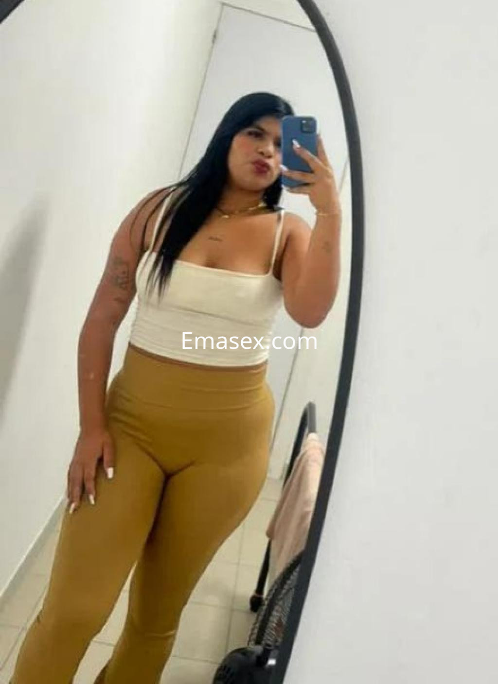 La puta en Barcelona se toma una selfie luciendo un top blanco y leggings amarillos en un espejo.