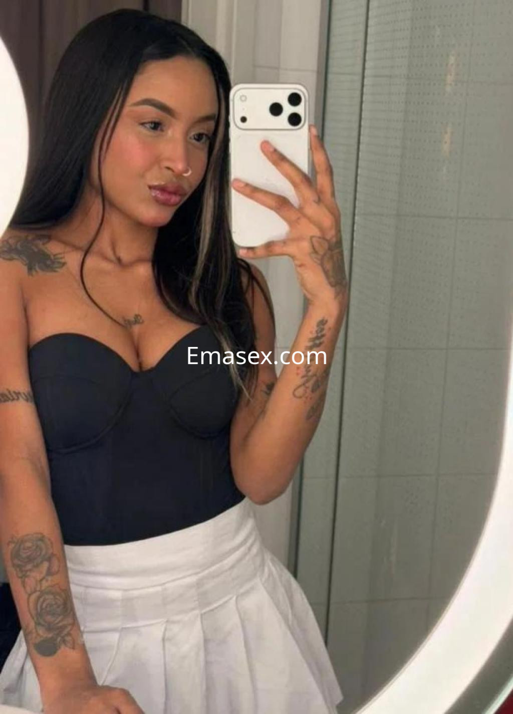 La puta se toma una selfie en Barcelona, luciendo un top negro y una falda blanca, con tatuajes visibles.