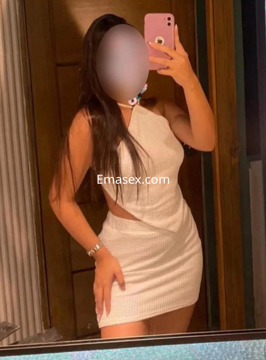 Escort en Cádiz con vestido blanco ajustado, posando frente al espejo, con cabello largo y lacio.