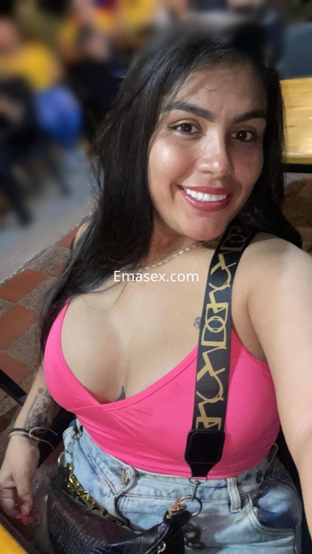 Escort en Pamplona con blusa rosa y tirantes, sonriendo mientras posa en un ambiente social.