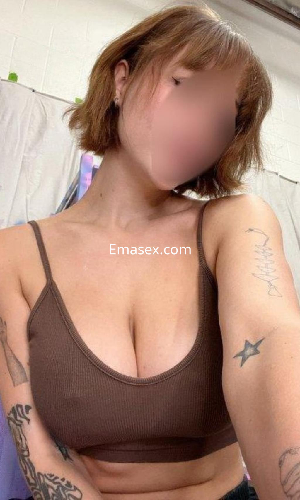 Escort en Pontevedra con cabello corto y castaño, luciendo un top marrón y mostrando varios tatuajes en el brazo.