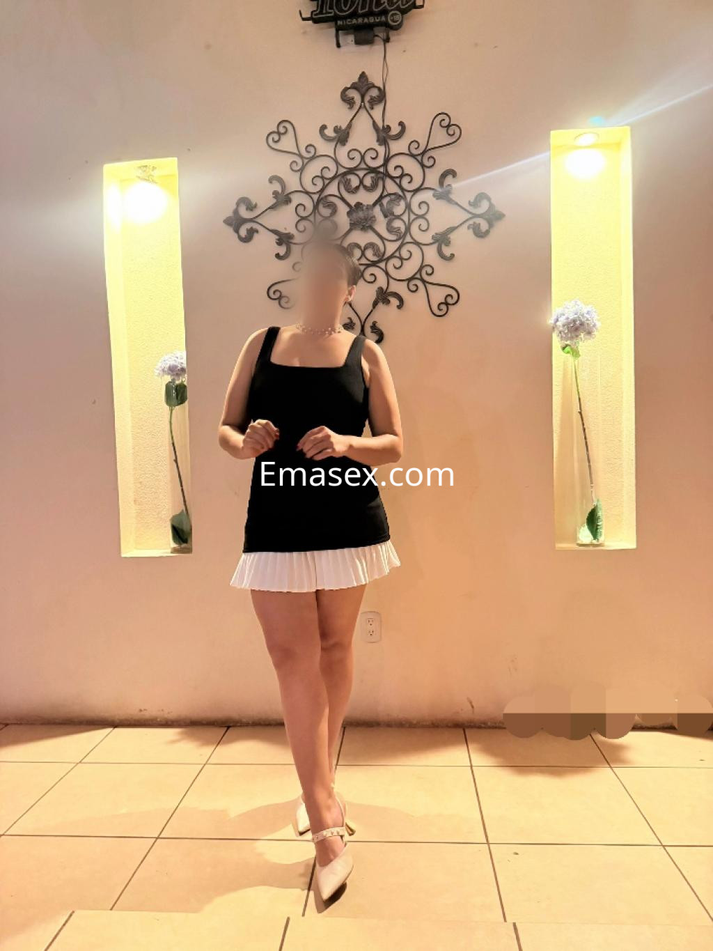 Escort en Vitoria viste un vestido negro con falda blanca y tacones, posando en un ambiente elegante.