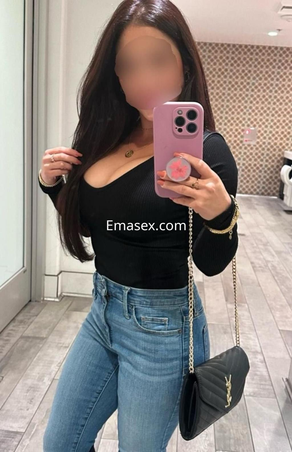 Puta en Cádiz posando en un espejo, viste un top negro ajustado y jeans claros, con una bolsa de mano.