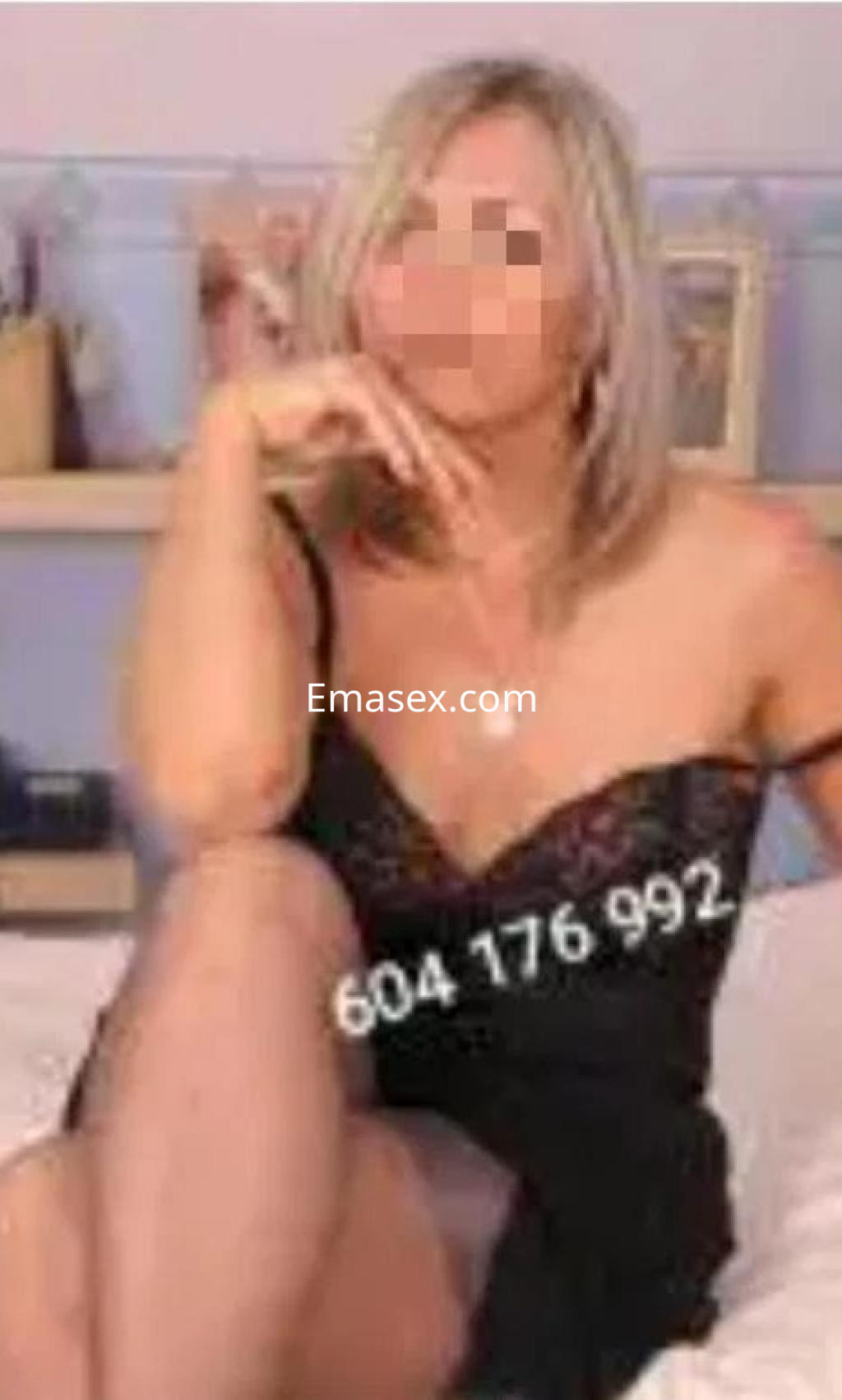 Escort en Coruña luciendo un vestido negro con encaje, sentada en una cama con un ambiente acogedor.