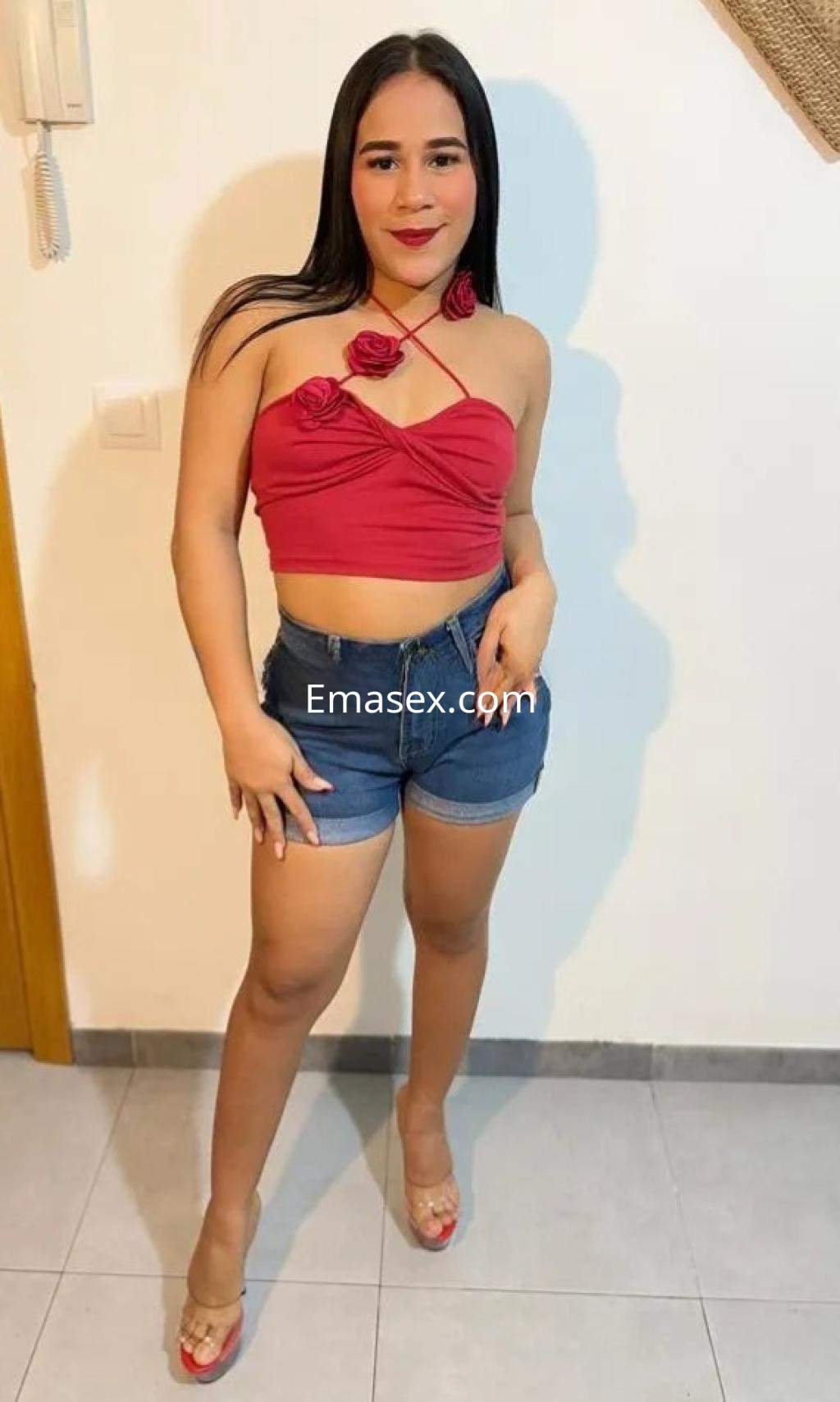 La puta luce un top rojo con flores, shorts de mezclilla y sandalias transparentes en un ambiente iluminado de Córdoba.