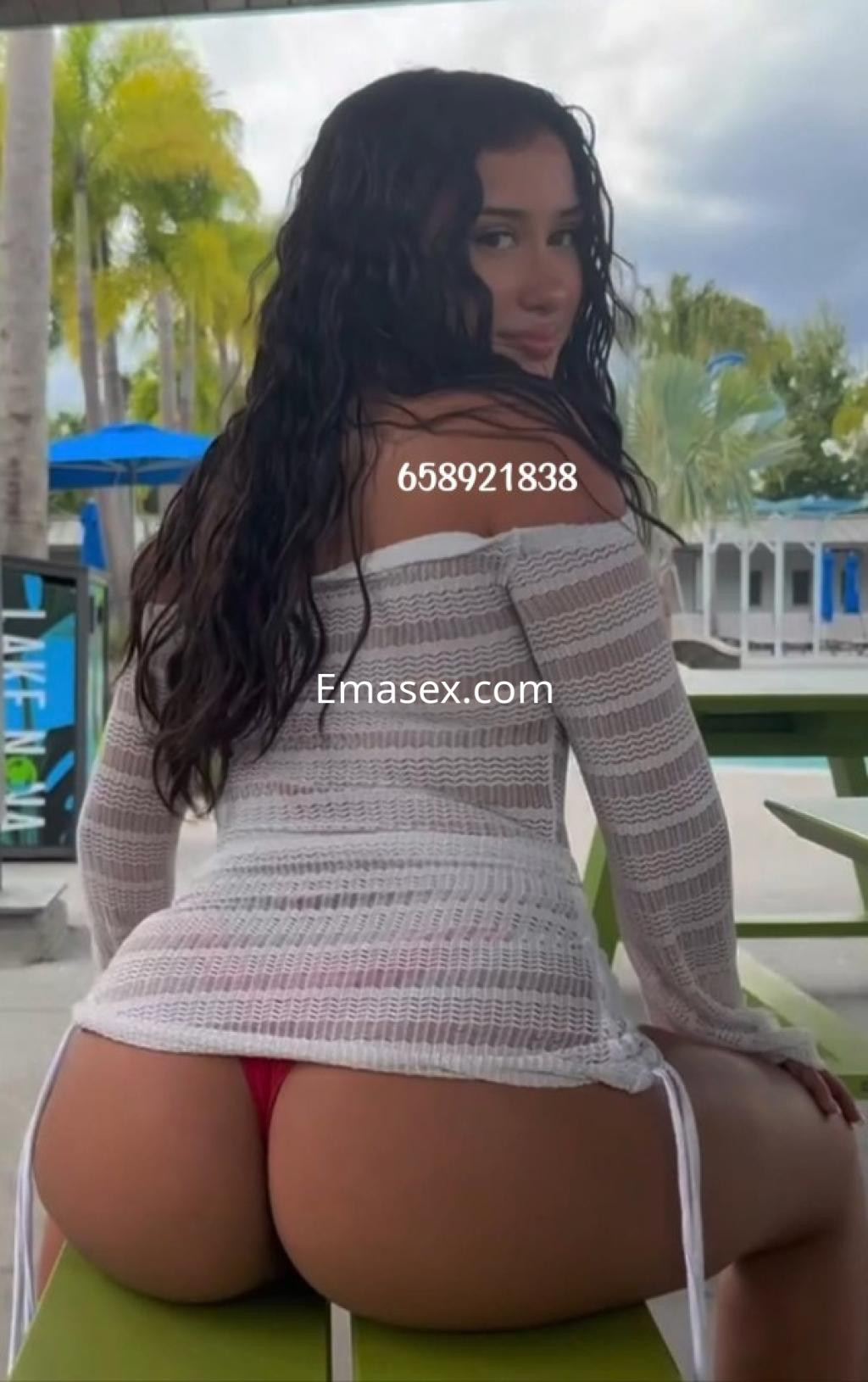 Puta en Coruña se sienta en una mesa al aire libre, luciendo una blusa blanca y bikini rojo.