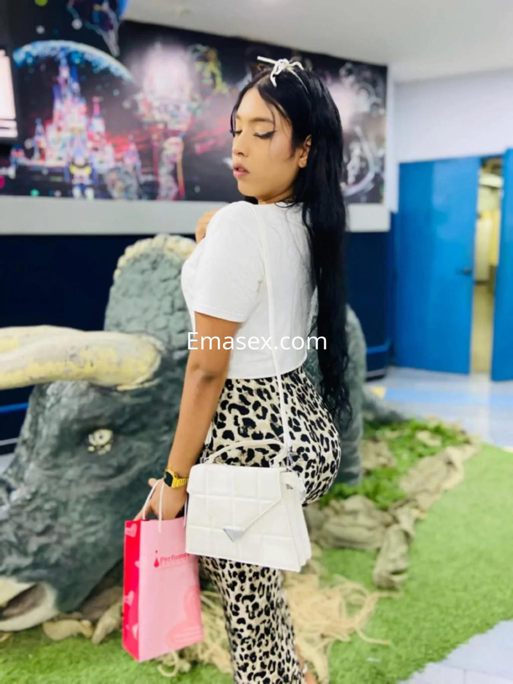 Escort en Granada con cabello largo y oscuro, viste una blusa blanca y leggins de leopardo, posando de perfil.