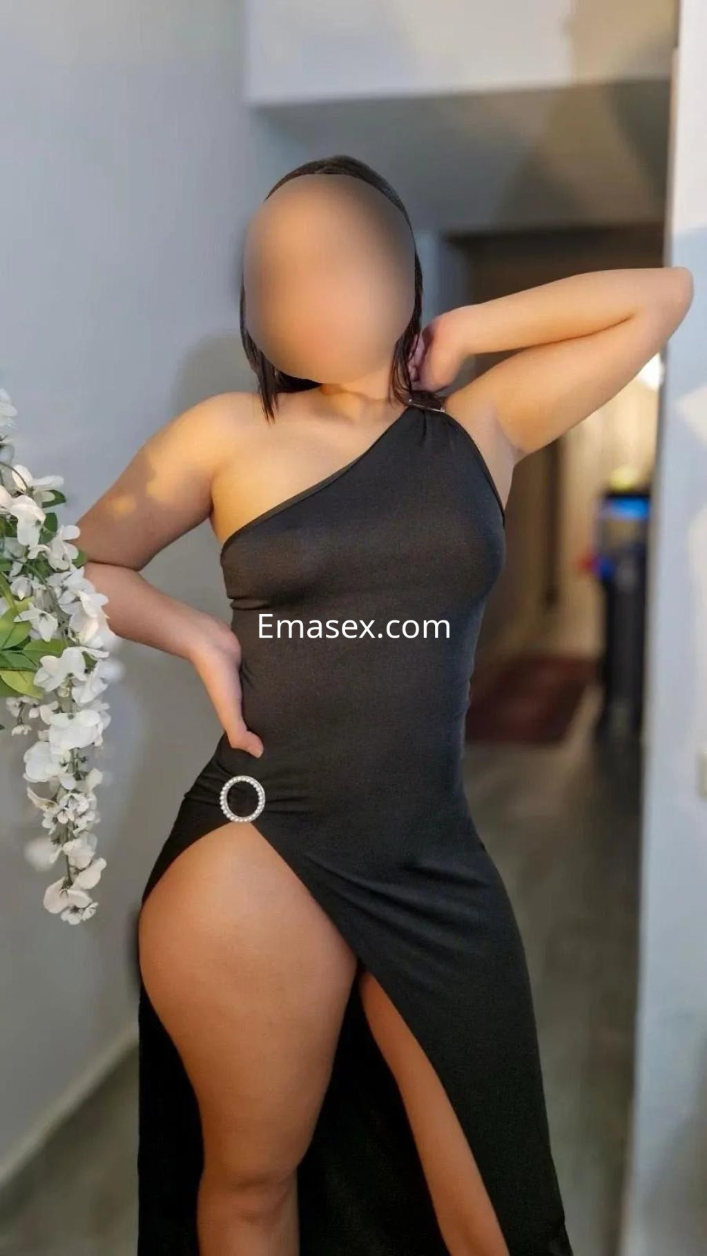 Puta en Madrid luciendo un vestido negro de una sola manga con una abertura lateral, posando con confianza.