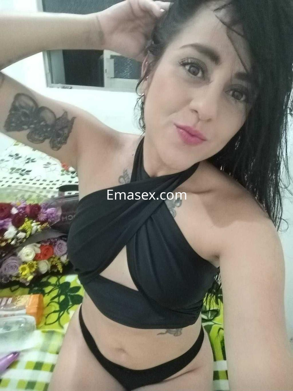 Escort en Pamplona posando con un top negro y bikini, con cabello oscuro y tatuajes visibles en los brazos.