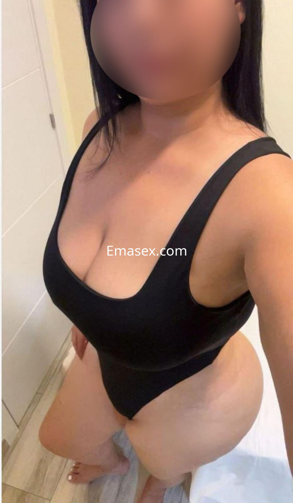 Escort en Ourense posando con un traje de baño negro, mostrando una figura curvilínea y cabello largo.