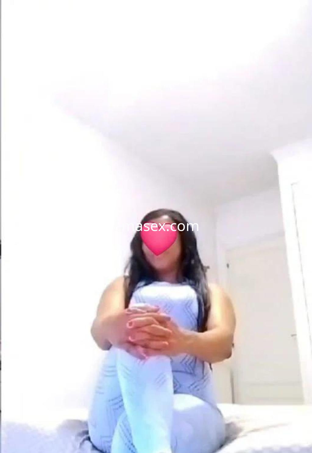 Puta sentada en una cama, vistiendo un conjunto ajustado de color claro, con el cabello largo y lacio en Salamanca.