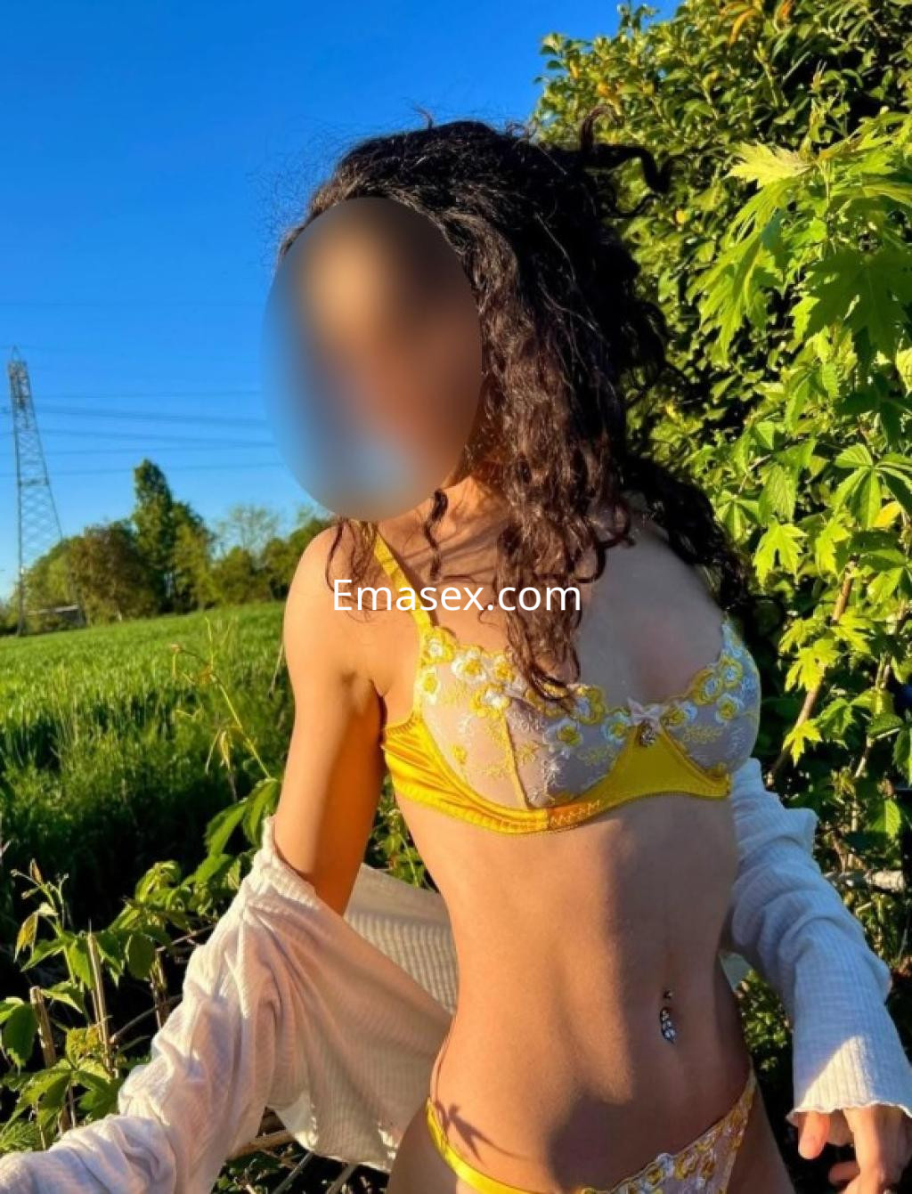 Escort en Tenerife, posando al aire libre con un conjunto de lencería amarilla y un abrigo claro sobre los hombros.