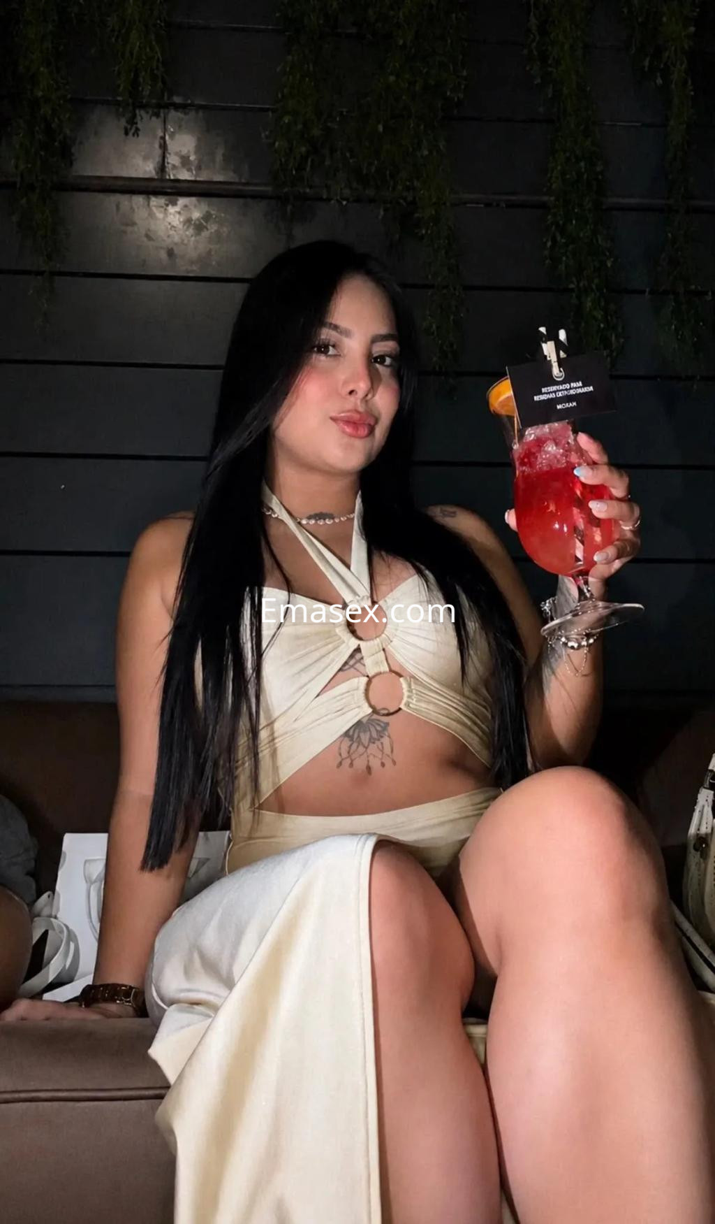 Puta de Zaragoza con cabello largo y oscuro, viste un top claro y sostiene un cóctel en un ambiente elegante.