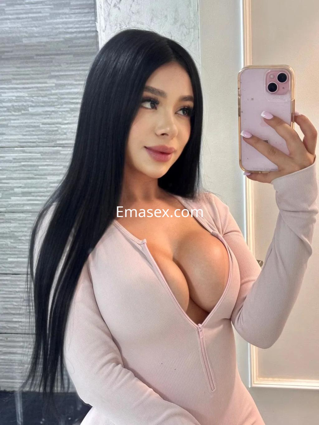 Escort de Zaragoza con cabello largo y lacio, usando un vestido ajustado de color rosa claro y posando frente al espejo.